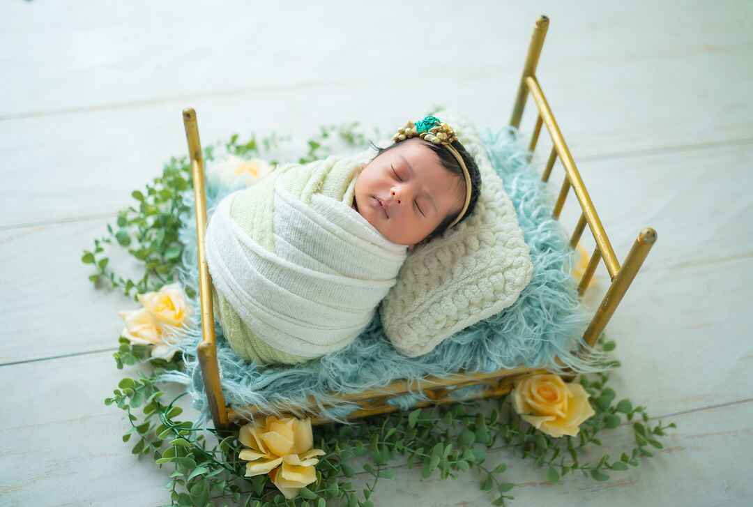 The perfect baby photography setup—tiny floral bed, soft white dress, and a sleeping baby girl.